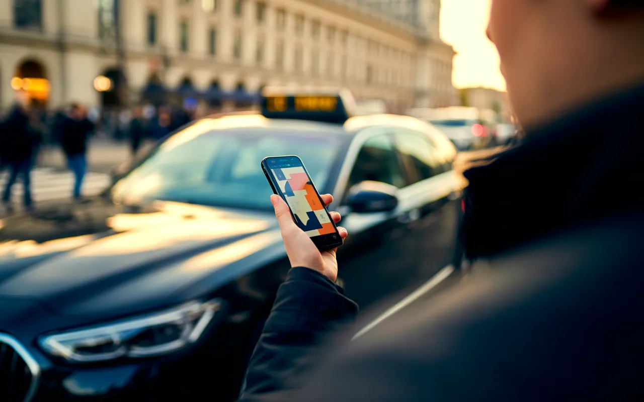 Smartphone en main au premier plan, taxi moderne noir (voyant vert) approche devant la Gare du Nord à Paris, heure dorée et bokeh doux; taxi gare du nord, réservation facile 2025.